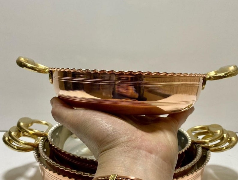 K&ouml;nnte beinhalten: Ein Satz aus drei Kupferservier-Schalen mit goldenen Griffen. Die Schalen sind ineinander verschachtelt und haben einen dekorativen gewellten Rand.
