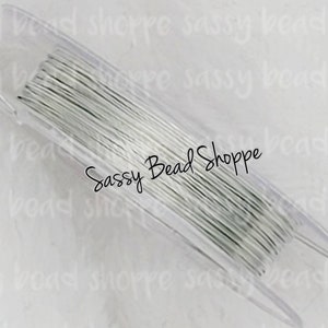 May include: A spool of silver-colored beading wire in a clear plastic container. The container has the text "Sassy Bead Shoppe" printed on it.
