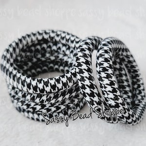 May include: A set of five black and white patterned elastic hair ties. The pattern is a houndstooth design.