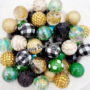 May include: A collection of colorful and patterned beads, including green, gold, black, and white. The beads are made of various materials, such as plastic, glass, and glitter. The beads are arranged in a pile, and some of them are overlapping. The beads are perfect for making jewelry, crafts, and other projects.