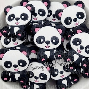 May include: A bowl filled with black and white panda-shaped silicone charms with pink accents. The charms have a cute cartoon design and are perfect for adding a playful touch to crafts and accessories.