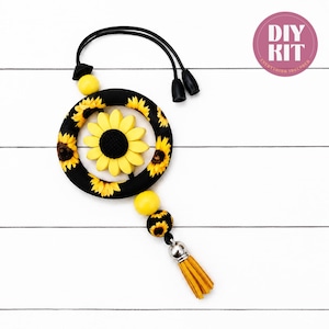 May include: A DIY kit featuring a black circular frame decorated with yellow sunflower patterns, a central yellow sunflower, yellow and sunflower-patterned beads, a black cord with two black end caps, and a yellow tassel with a silver-toned metal cap.