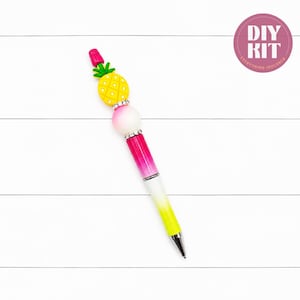 May include: A pen featuring a yellow pineapple topper, a white spherical bead, and a pink-to-yellow gradient barrel. The design includes silver-toned rhinestone spacers and a pink cap. A circular pink badge in the corner displays the text DIY KIT.