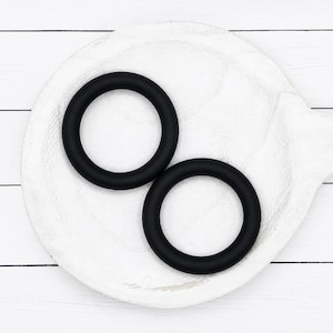 May include: Two smooth, matte black circular rings with a uniform thickness. The rings are solid in color and feature a simple, continuous round shape. These two identical circular components are presented together, showcasing a clean, dark finish.