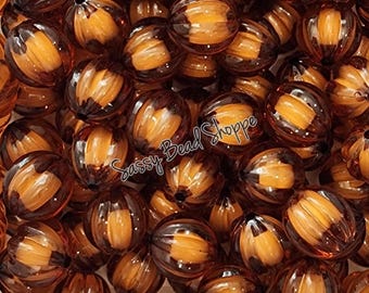 May include: A large pile of amber-colored plastic pumpkin beads. The beads have a ribbed texture and are perfect for fall crafts.