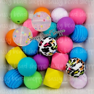 K&ouml;nnte beinhalten: Eine Sammlung bunter, runder und quadratischer Silikonperlen in verschiedenen Mustern, darunter Leopardenmuster, Punkte und Streifen. Die Perlen sind in einer wei&szlig;en Sch&uuml;ssel angeordnet. Der Text "Sassy Bead Shoppe" ist in der Mitte des Bildes sichtbar.