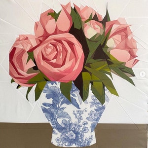 Puede incluir: Un ramo de peonías de papel rosa en un jarrón con estampado floral azul y blanco. El jarrón es una pieza de arte hecha a mano.