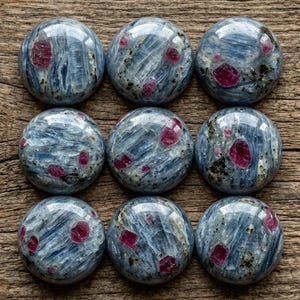 May include: Nine circular cabochons arranged in a three-by-three grid. Each cabochon features a polished, smooth surface with a blue and grey fibrous texture, interspersed with distinct, embedded deep pink to red crystalline inclusions.