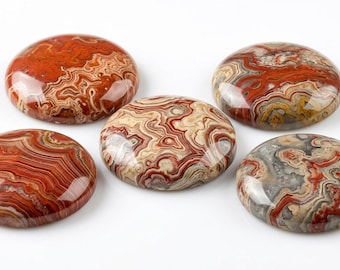 May include: Five polished, oval-shaped stones with intricate patterns. The stones display a mix of red, brown, beige, and gray hues, with swirling and layered designs. The surfaces are glossy, reflecting light.