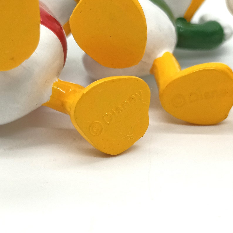 Pode incluir: Close-up dos p&eacute;s amarelos de v&aacute;rias figuras do Pato Donald. Os p&eacute;s s&atilde;o estampados com o logotipo da Disney. As figuras s&atilde;o brancas, vermelhas e verdes.