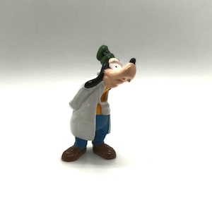 Pode incluir: Uma pequena e colorida figura do Pateta, um personagem de desenho animado da Disney. Pateta est&aacute; vestindo um jaleco branco, cal&ccedil;as azuis, sapatos marrons e um chap&eacute;u verde. Seu grande focinho bronzeado &eacute; proeminente e ele parece estar olhando para baixo.