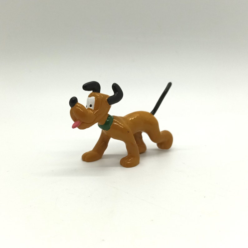 Pode incluir: Uma pequena figura de Pluto marrom com orelhas pretas e uma cauda preta. O c&atilde;o tem uma coleira verde e uma l&iacute;ngua rosa. A figura est&aacute; em posi&ccedil;&atilde;o de caminhada.