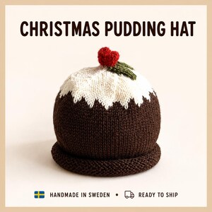 May include: A knitted hat designed to resemble a Christmas pudding, featuring a dark brown base, a white top section with a jagged edge, and a small red berry with a green leaf on the crown. The text CHRISTMAS PUDDING HAT is printed above.