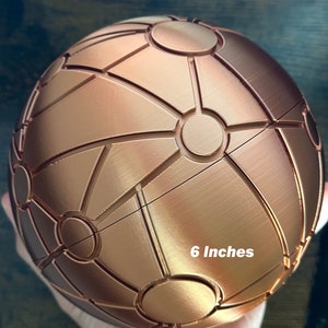 May include: A 6-inch copper-coloured sphere with a geometric pattern. The sphere is made of a smooth, metallic material and has a shiny finish.