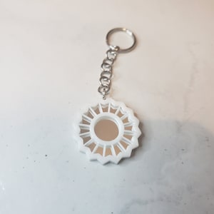 Op de afbeelding: Witte sleutelhanger met een ronde spiegel in het midden. De spiegel is omgeven door een wit, stervormig frame.