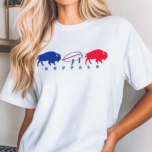 May include: White t-shirt with a blue and red buffalo graphic and the word "BUFFALO" printed on the front.
