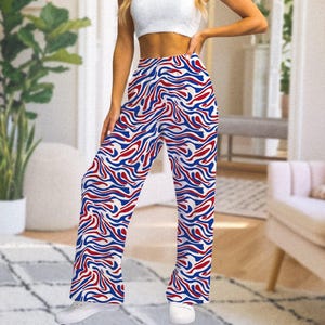 Op de afbeelding: Broek met wijde pijpen met een levendig patroon van rode en blauwe golvende lijnen op een witte achtergrond. De broek heeft een hoge taille en is gemaakt van een lichte stof. De broek maakt deel uit van een casual kledingcollectie.