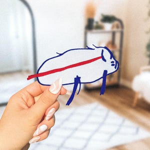 May include: A hand holds a blue and white drawing of a pig with a red line across its body. The pig is drawn in a simple, childlike style.