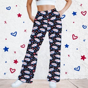 May include: Black high-waisted wide-leg pants featuring a repeating pattern of white buffalo silhouettes with red and blue accents, small red and blue hearts, and tiny footballs. The pants have a straight-leg cut and a fitted waistband.