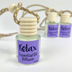 May include: A small clear glass bottle with a wooden lid and a purple label that says "Relax Essential Oil Diffuser 0.2 oz". The bottle is hanging from a brown and gold string.
