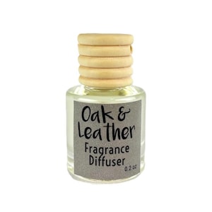 May include: A small, clear glass fragrance diffuser bottle with a light-colored wooden cap. The label reads "Oak & Leather Fragrance Diffuser" and "0.2 oz". The bottle contains a clear liquid.