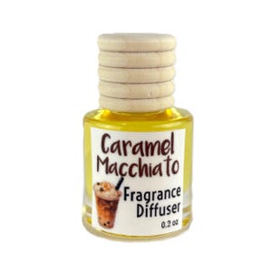 May include: A small glass fragrance diffuser bottle with a wooden cap. The label reads "Caramel Macchiato Fragrance Diffuser" with an illustration of a caramel macchiato drink. The bottle contains 0.2 oz of liquid.