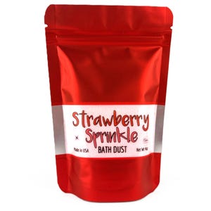 May include: A red, shiny pouch of strawberry-scented bath dust. The product name "Strawberry Sprinkle" is written in a playful font, with the words "Bath Dust" below. The package states "Made in USA" and the net weight is 4 oz.
