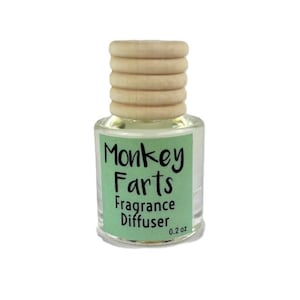 May include: A small glass fragrance diffuser with a wooden cap. The label reads "Monkey Farts Fragrance Diffuser" in black text on a light green background. The bottle contains 0.2 oz of liquid.