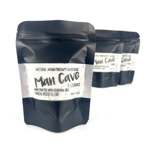 May include: Three black pouches with white labels containing bath salts. The label reads "Natural Aromatherapy Bath Soak Man Cave 1-2 Soaks Hand Crafted with Essential Oils Sandalwood & Lime Net 2.5 oz"