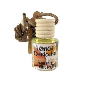 May include: A small, clear glass bottle with a wooden cap and a rope loop, labeled "Lemon Poundcake Fragrance Diffuser." The bottle contains a yellow liquid and is designed for use as an air freshener. The label features a picture of lemon pound cake.