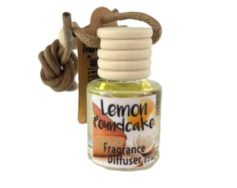 May include: A small, clear glass bottle with a wooden cap and a rope loop, labeled "Lemon Poundcake Fragrance Diffuser." The bottle contains a yellow liquid and is designed for use as an air freshener. The label features a picture of lemon pound cake.