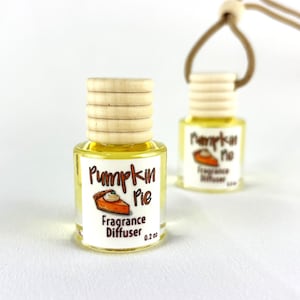 May include: Two small glass fragrance diffusers with wooden caps and a string for hanging. The labels read "Pumpkin Pie Fragrance Diffuser 0.2 oz" with a graphic of a pumpkin pie slice. The liquid inside is yellow.
