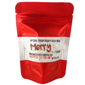 May include: A red pouch with a clear window containing white bath soak. The text "Merry" is displayed in a festive font. The label reads "Natural Aromatherapy Bath Soak" and "Hand Crafted with Essential Oils". The net weight is 26 oz.