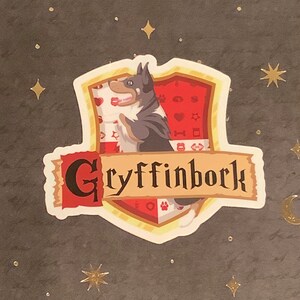 May include: A sticker featuring a cartoon dog with a red, white, and gold shield. The shield has a paw print and other symbols. The text "Gryffinbork" is on a red banner.