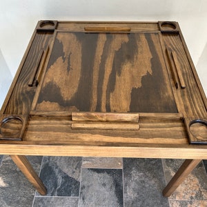 May include: A dark brown wooden game table with four cup holders and a built-in scorekeeper. The table has a smooth, polished finish and is perfect for playing games like dominoes or cards.