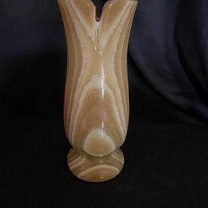 May include: A light brown, carved, alabaster vase with a unique, split-top opening. The vase has a smooth, polished finish and intricate, swirling patterns.