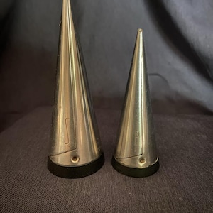 May include: A set of two silver cone-shaped salt and pepper shakers with black plastic bases. The shakers have a brushed metal finish and are marked with "S" and "P" for salt and pepper.