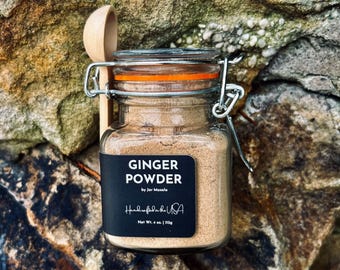 May include: A glass jar with a metal lid and a wooden spoon. The jar contains ginger powder and has a black label that reads "Ginger Powder by Jar Masala Handmade in the USA Net Wt. 4 oz. | 113g".