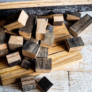 May include: A collection of small, wooden blocks with a natural, weathered appearance. The blocks are various shades of brown and gray, with some showing a darker, charred effect on their surfaces. They are scattered on a light brown wooden surface.