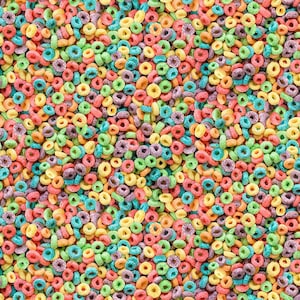 May include: A close-up of colourful, ring-shaped cereal pieces. The cereal pieces are in a variety of colours, including red, yellow, green, purple, and blue. The image is a full frame, with no negative space.