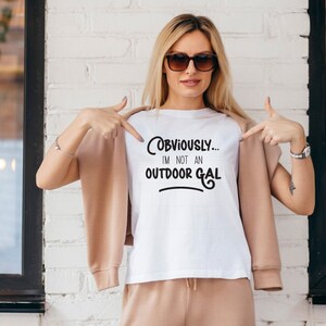 May include: White t-shirt with black text that reads "OBVIOUSLY... I'M NOT AN OUTDOOR GAL".