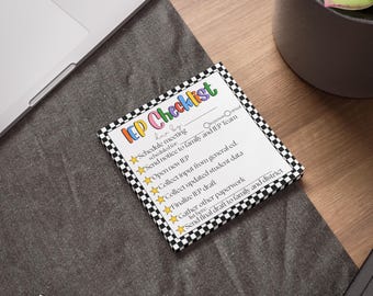 May include: A square IEP Checklist notepad with a colorful title and a black and white checkered border. The checklist includes tasks like scheduling meetings and sending notices. The notepad is on a dark gray surface.