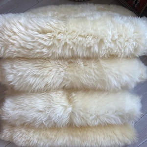 May include: Four white sheepskin rugs stacked on top of each other. The rugs are soft and fluffy, and they would be perfect for adding a touch of warmth and comfort to any room.