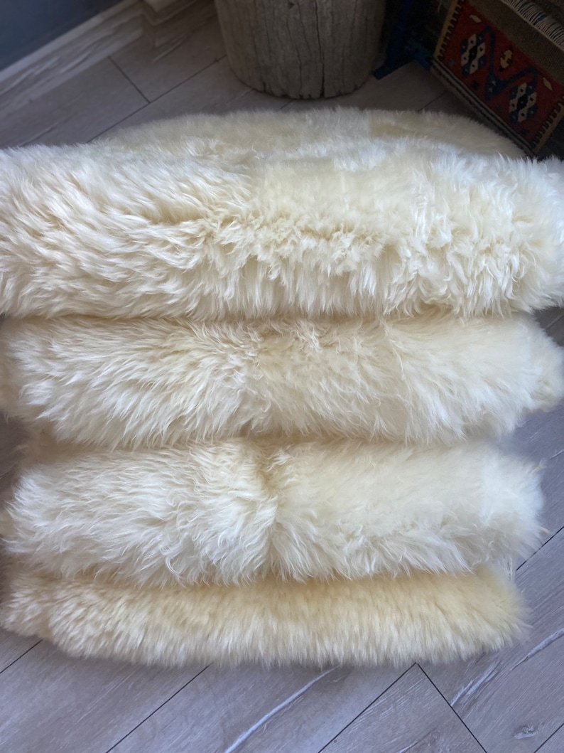 May include: Four white sheepskin rugs stacked on top of each other. The rugs are soft and fluffy, and they would be perfect for adding a touch of warmth and comfort to any room.