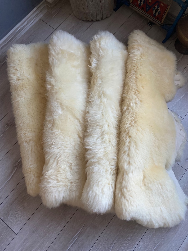 May include: Four white sheepskin rugs laid out on a wooden floor. The rugs are soft and fluffy, and they would be perfect for adding a touch of warmth and comfort to any room.