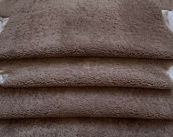 May include: A stack of brown sheepskin hides with a soft, fuzzy texture. The hides are folded and arranged in a neat pile.