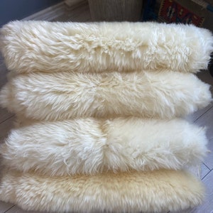 May include: Four white sheepskin rugs stacked on top of each other. The rugs are soft and fluffy, and they would be perfect for adding a touch of warmth and comfort to any room.