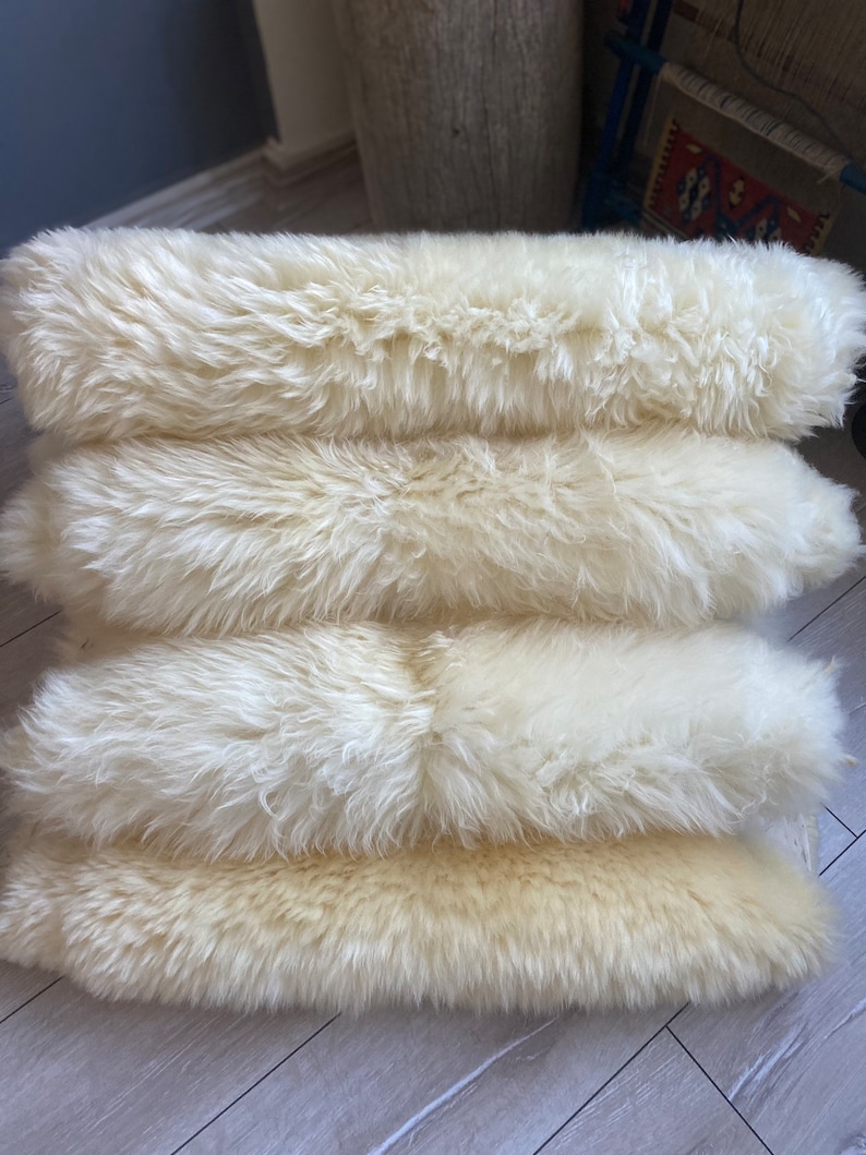 May include: Four white sheepskin rugs stacked on top of each other. The rugs are soft and fluffy, and they would be perfect for adding a touch of warmth and comfort to any room.
