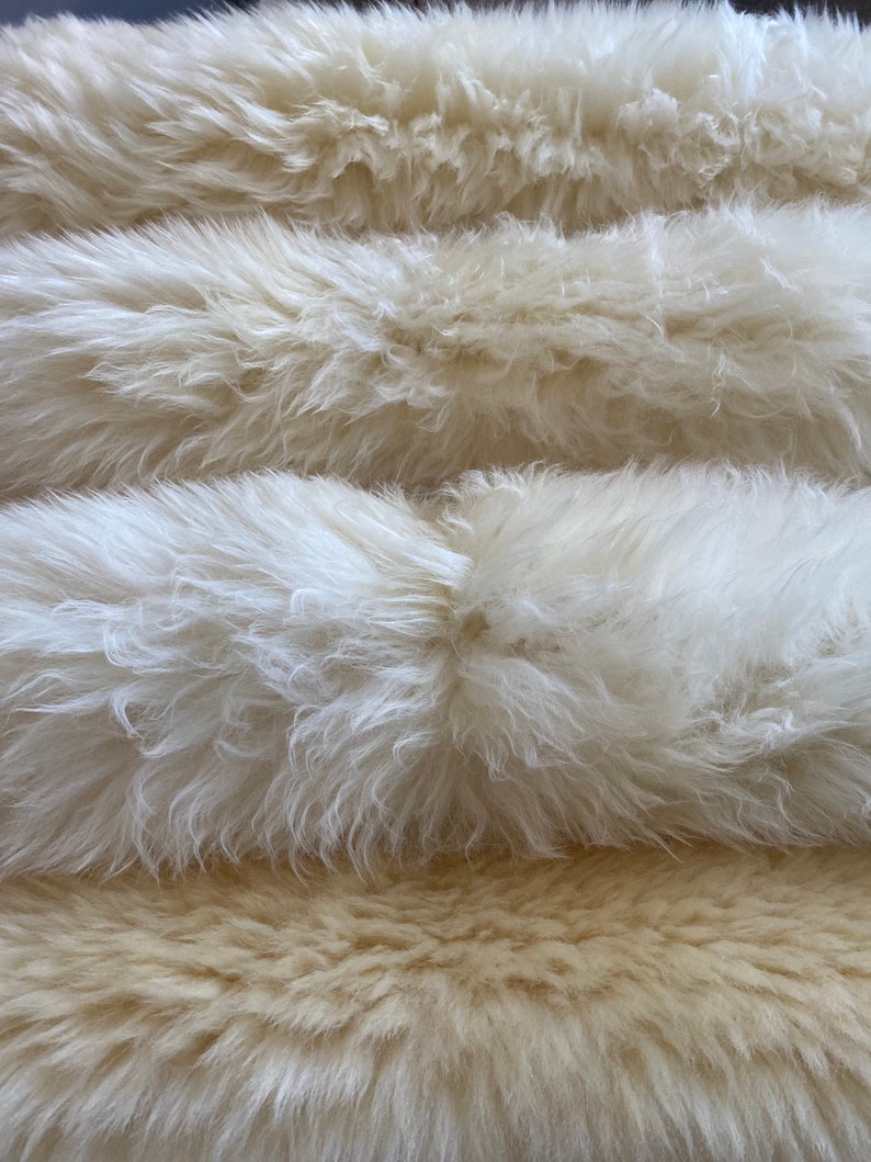 May include: A stack of three fluffy white faux fur rugs. The top two rugs are white and the bottom rug is a light beige colour.