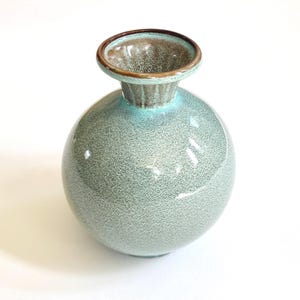 May include: A small, round, light blue ceramic vase with a brown rim. The vase has a speckled texture.